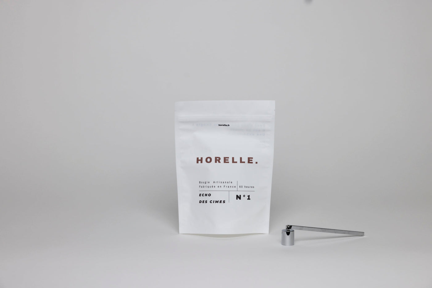 La mouchette et l'éteignoir Horelle posés à côté d'une recharge de cire, les deux outils qui empêchent une bougie de fumer