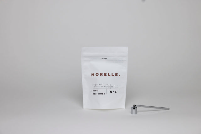 La mouchette et l'éteignoir Horelle posés à côté d'une recharge de cire, les deux outils qui empêchent une bougie de fumer