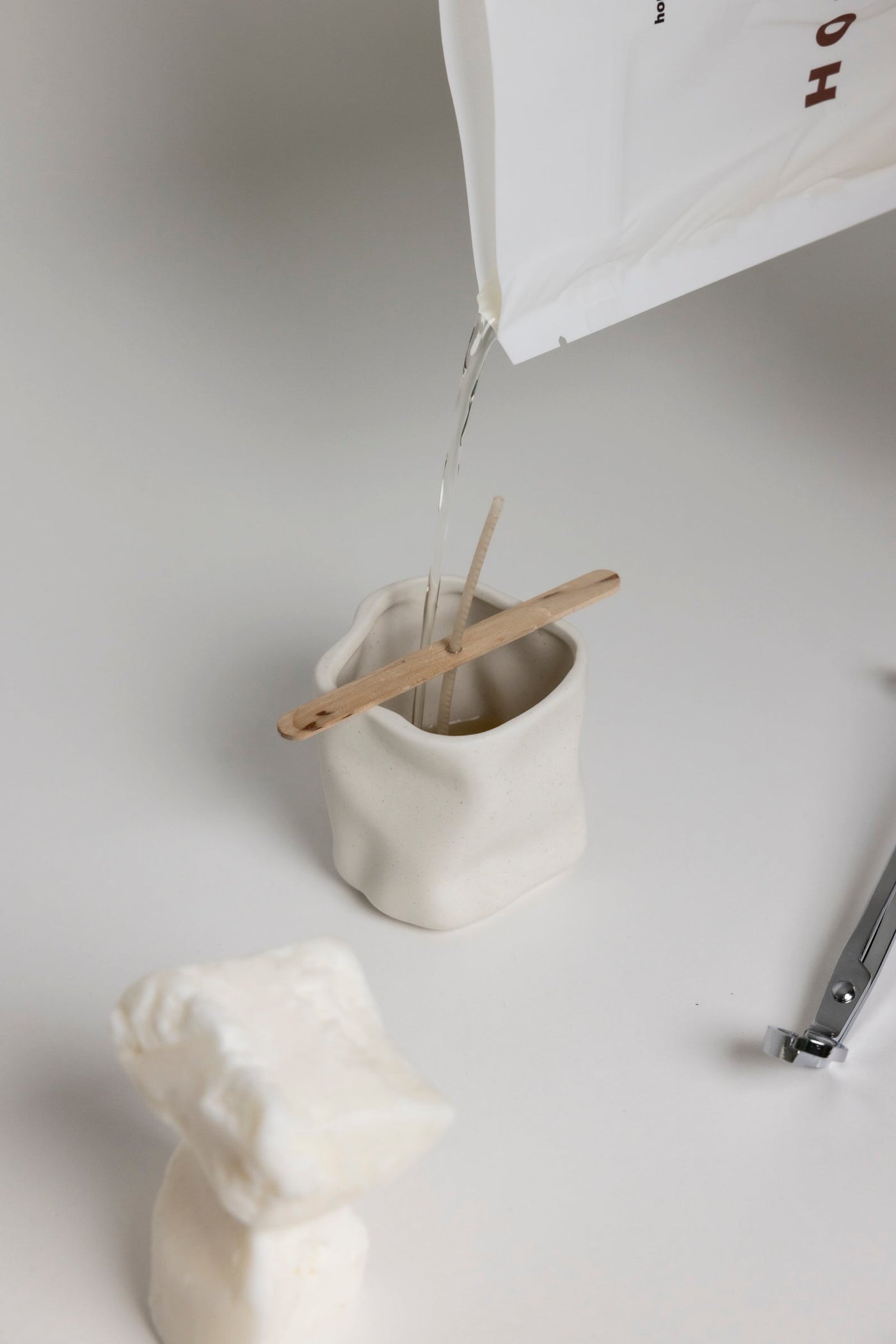 La cire liquide versée du sachet dans un contenant en céramique, mèche tenue par une pique en bois