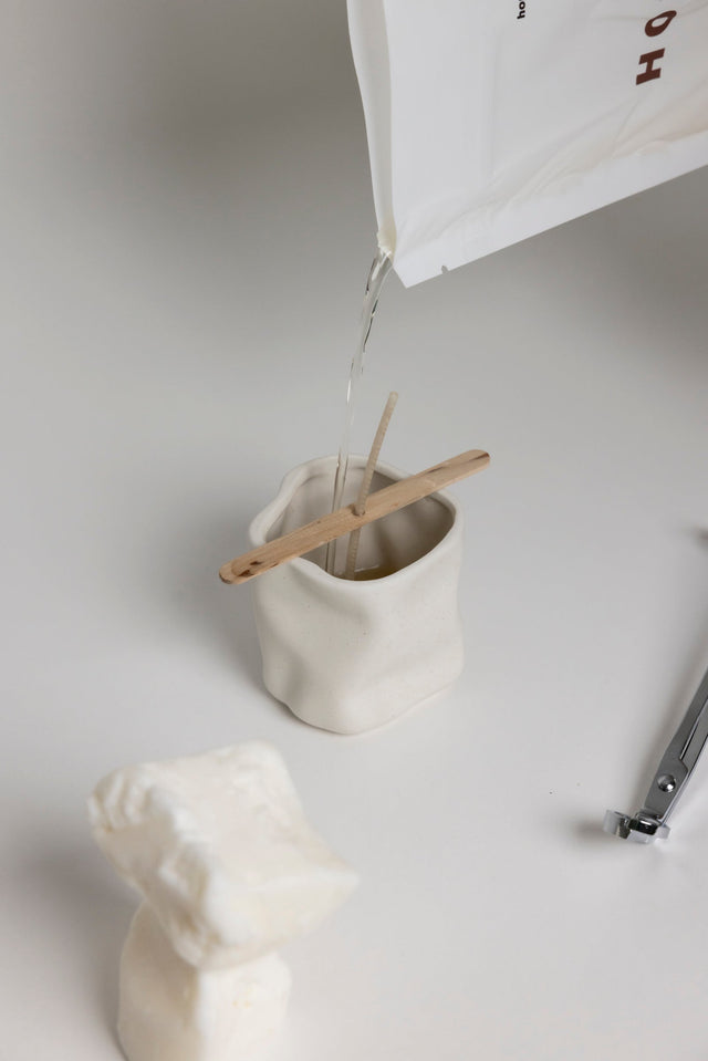 La cire liquide versée du sachet dans un contenant en céramique, mèche tenue par une pique en bois