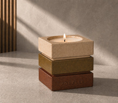 Le contenant signature Horelle, trois strates de ceramique emaillee, sable, olive et terre rouge, bougie allumee